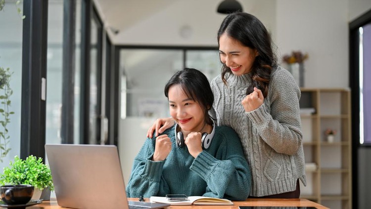 1449528841 Happy and cheerful Asian businesswomen or business employees clenched fist, looking at laptop screen, celebrating their project success together. victory, winning, good news