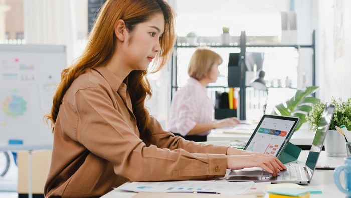 Ilustrasi seorang perempuan yang terlihat sedang bekerja di meja kerjanya.