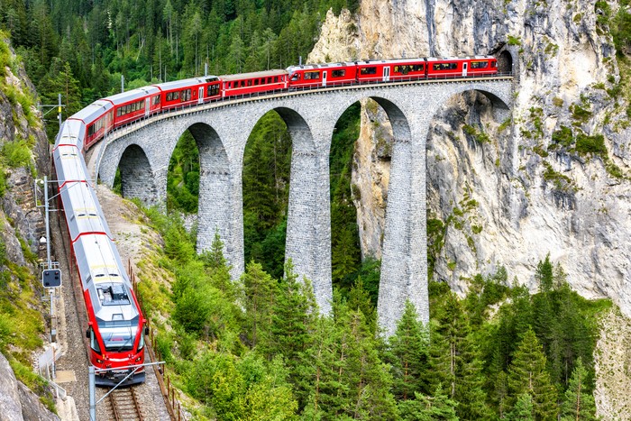 Landwasser Viaduct in Filisur, Switzerland. It is famous landmark of Swiss. Red express train on high bridge in mountains. Scenic view of amazing railway in summer. Concept of travel in Alpine Europe.
