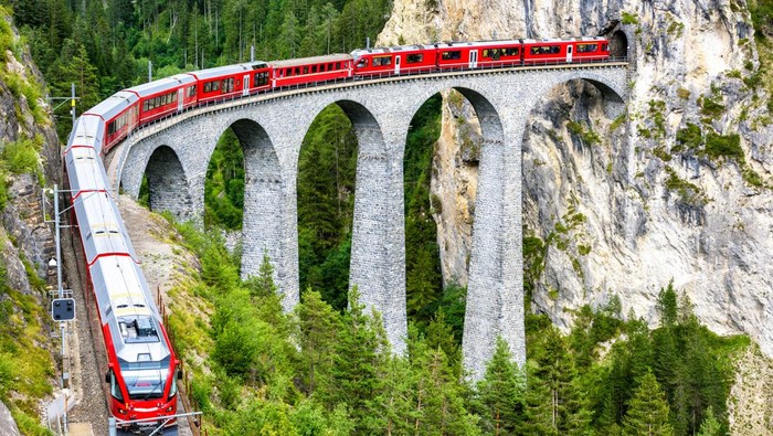 Landwasser Viaduct in Filisur, Switzerland. It is famous landmark of Swiss. Red express train on high bridge in mountains. Scenic view of amazing railway in summer. Concept of travel in Alpine Europe.
