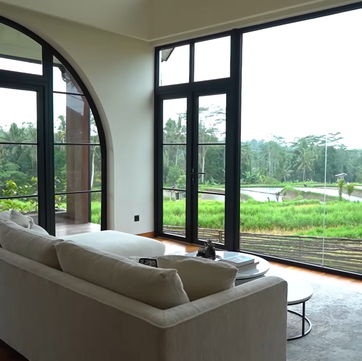 <p>Ruang tamu rumah ini menyajikan pemandangan indah dari sawah sambil bersantai di sofa empuk. "Biasanya kalau kita punya sofa, kita selalu arahin ke TV. Tapi di rumah ini, kita arahin ke sawah. Ini adalah <em>entertainment</em> utamanya," ucap Christian. (Foto: YouTube Titi dan Tian)</p>