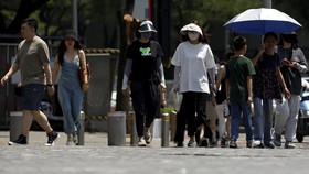 People wearing sun-protective clothing cross a road amid a yellow alert for heatwave in Beijing, China June 5, 2023. REUTERS/Florence Lo