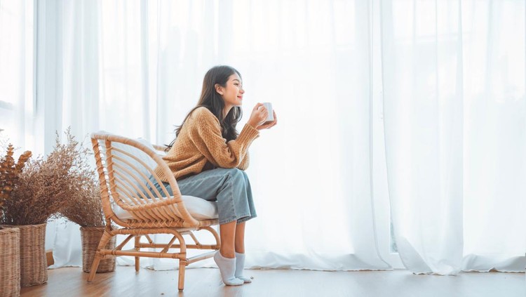 1443051692 Happy asian woman relaxing drinking hot coffee or tea in holiday morning vacation on armchair at home, Cosy scene, Smiling pretty woman drinking hot tea in autumn winter. copy space.