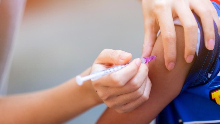 Hands of doctor in medical gloves injecting vaccine to a child patient. Doctor giving muscular injection to little child in arm. Vaccination healthcare concept.
