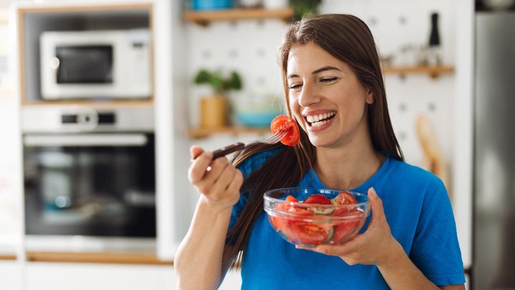 1402191343 Happy woman eating a salad in the kitchen