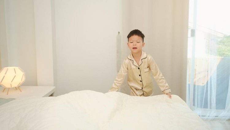 Happy little Asian kindergarten boy child make up his room and fold the blanket in bedroom at home, Kid make the bed, straightens a blanket on a large bed with good mood, Selective focus at the boy