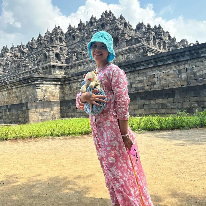 <p>Jizzy turut membawa boneka beruang berwarna krem ketika mengunjungi candi. Ia juga terlihat mengganti alas kakinya dengan sandal tradisional yang terbuat dari anyaman. (Foto: Instagram: @marshatimothy)</p>