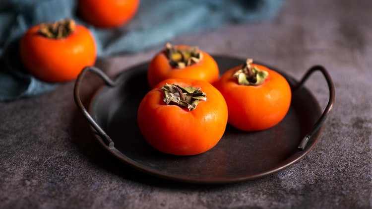 Persimmon orange kaki fruit on a artistic metal plate in a rustic dark setup