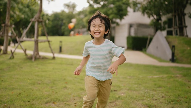 Playful boy running along in park on free day.