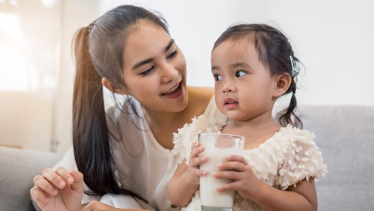 Young happy Asian mother and daughter coloring together at home with art tools and glass of milk.