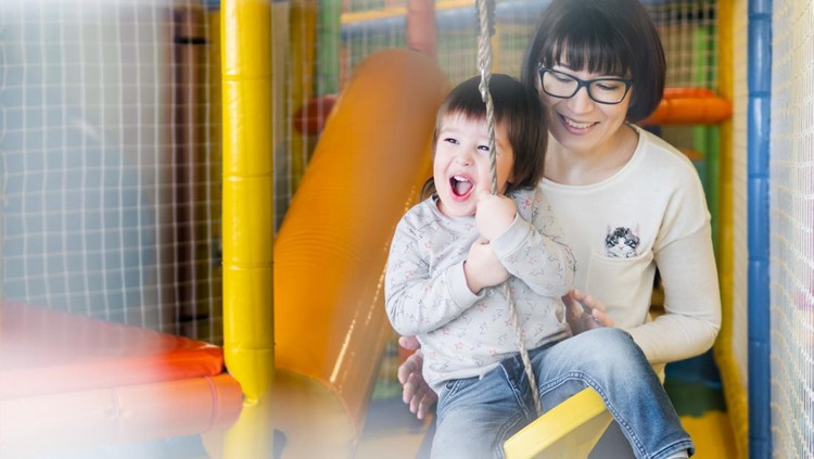 playground indoor di mall Toddler plays on rope swing with his mother or babysitter. Physical development for little children. Interior of kindergarten or nursery.