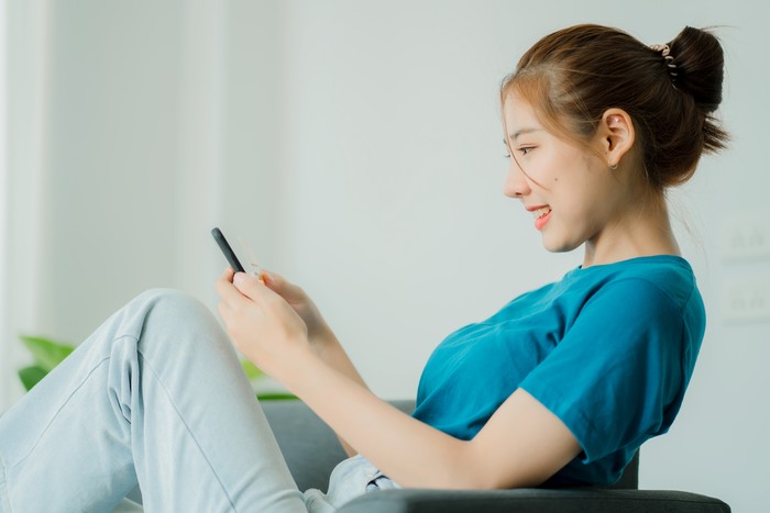 Cute and beautiful Asian woman lying on the sofa relaxing on the sofa playing social media happily at home.