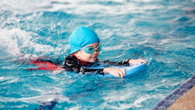Ilustrasi Baju Renang Muslimah Anak One girl wearing a swimsuit uses a foam pad to practice swimming in a swimming pool with a teacher. She happily and smiling.