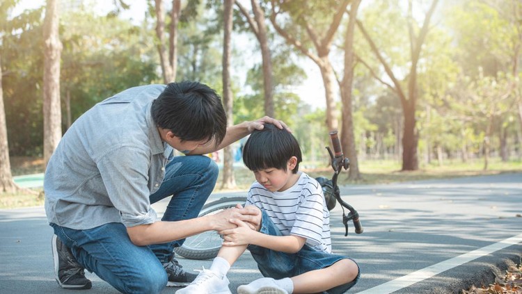 Young boy holds a sore leg that received a injury while playing outdoors.