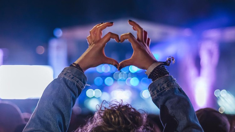 1394919041 Woman making heart shape with hands at music event