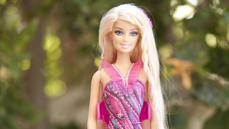 Cairo, Egypt - January 16, 2015:  Barbie doll is sitting outside on her chair and wearing a beautiful purple dress. Barbie is a fashion doll. Barbie on a green  nature background.