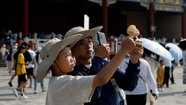Seorang pengunjung bertopi mengambil gambar es krim di Temple of Heaven, di tengah peringatan kuning untuk gelombang panas di Beijing, China 19 Juli 2023. (REUTERS/Florence Lo)