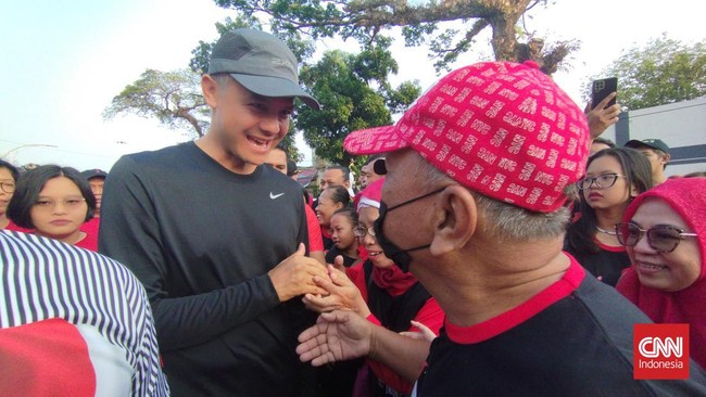 Gibran Rakabuming Raka memakai kemeja garis vertikal hitam-putih saat menemani Ganjar Pranowo di acara Jalan Sehat DPC PDIP Solo, Minggu (23/7).