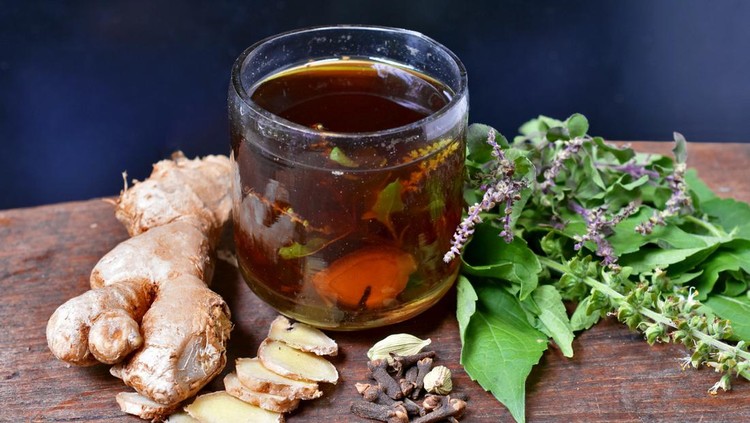 Ingredients in a small glass of Herbal Tea Ingredients are ginger, basil, cardamom, cloves on wooden table with black background