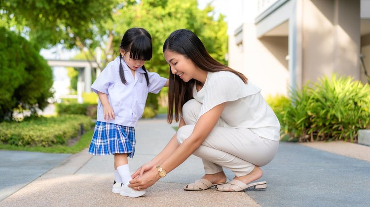 Asian mother helping her daughter put shoes on or take off at outdoor park getting ready to go out together or coming back home from school in happy family with kids concept&period;