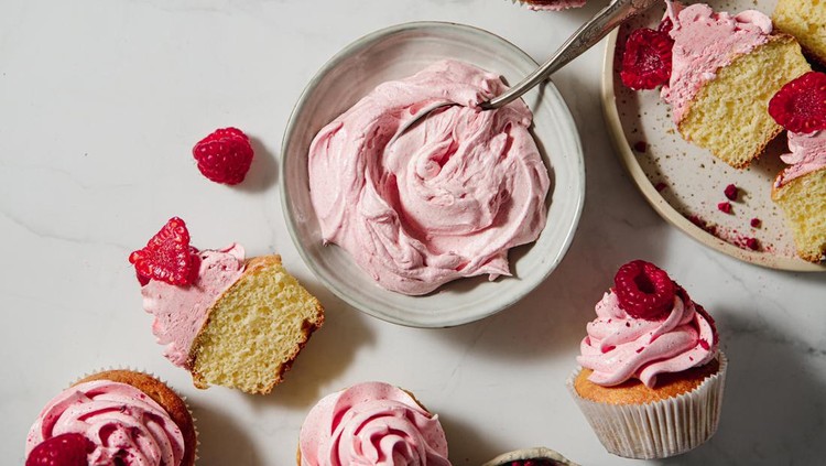 1369757617 Top view of a pink whipped cream in a bowl with half sliced raspberry cupcakes on table. Homemade raspberry cupcakes on kitchen table.