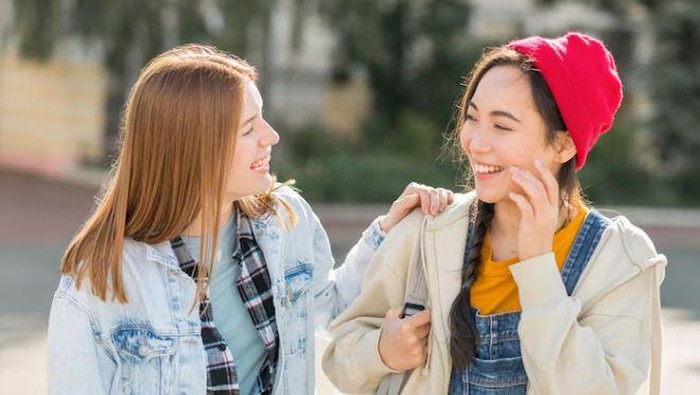 Dua perempuan sedang mengobrol sambil tertawa