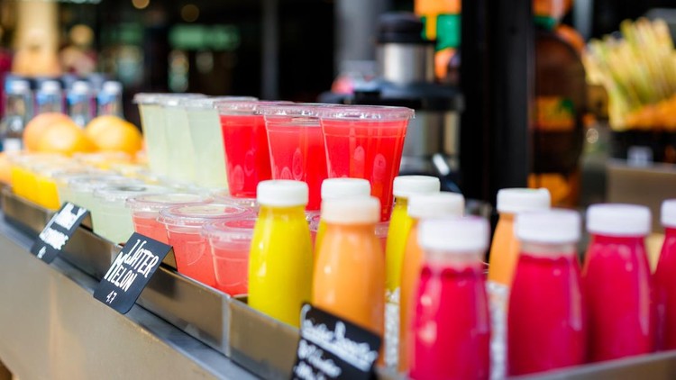 Close up color image depicting freshly made fruit juices and smoothies on display in a row and for sale at a food and drink market in London, UK. Selective focus on the plastic cups containing the fresh smoothies. Room for copy space.