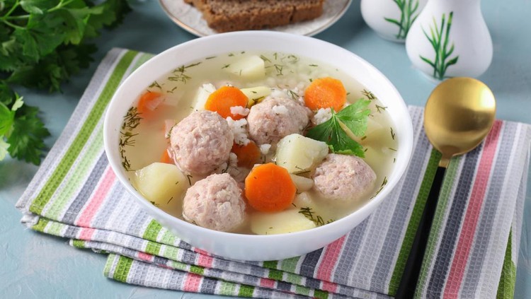 Soup with chicken meatballs, rice and vegetables in a white bowl on a blue background