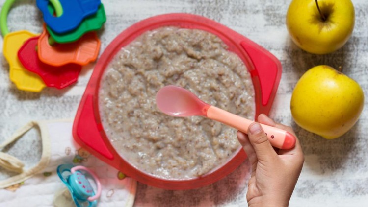 Top view of hand of child holding spoon to eat milk buckwheat porridge