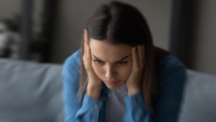 1309798024 Close up unhappy woman suffering from strong headache and dizziness, depressed young female blurry motion background, sitting on couch alone, touching temples, feeling pain, unwell and unhealthy