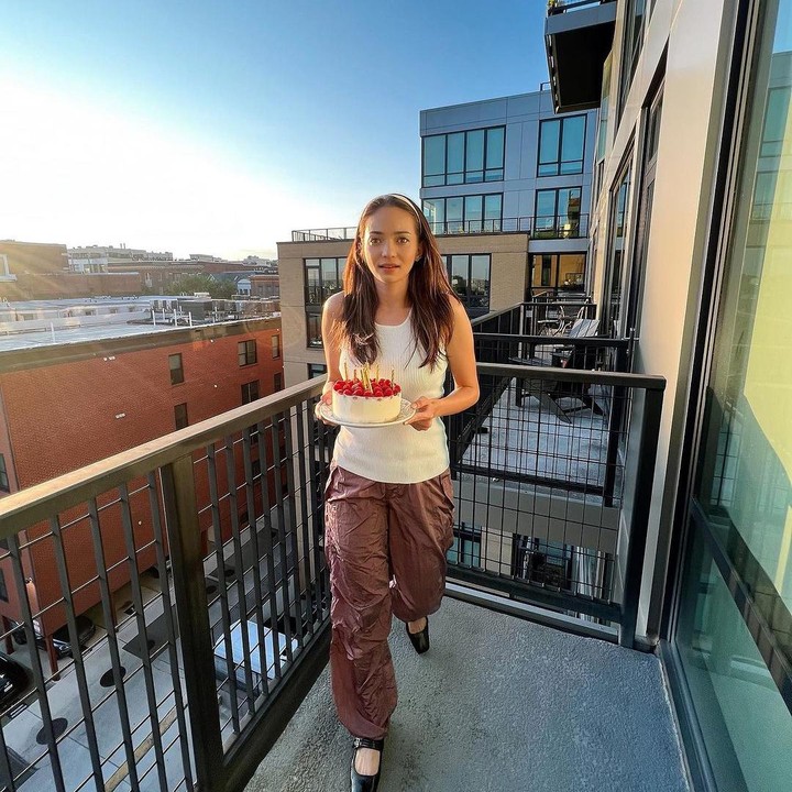 <p>Enzy tampak sedang berada di balkon saat berpose dengan kue ulang tahunnya. Selain pakaian casual, Enzy terlihat mengenakan <em>make up</em> natural dengan menggunakan aksesoris bando di rambut. (Foto: Instagram @enzystoria)</p>
