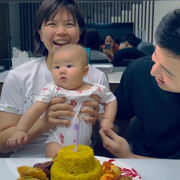 <p>Greysia terlihat memangku anak pertamanya, Jessia Selah Djimin, yang terlihat menggemaskan. Kemudian, sang suami membawa nasi kuning yang dibentuk seperti kue bertingkat dengan lilin menyala di atasnya. (Foto: Instagram @greyspolii dan @felixdjimin)<br /><br /><br /></p>