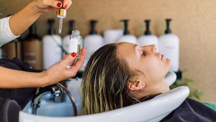1392177469 Beautiful young woman getting her hair washed in hair salon. She is relaxing with her eyes closed while the hairdresser massages her scalp and washes her hair with shampoo, hair treatment and water.