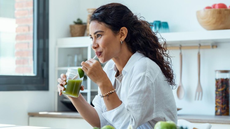 Ilustrasi diet Shot of pretty woman looking to sideways while drinking fruit detox juice in the kitchen at home.