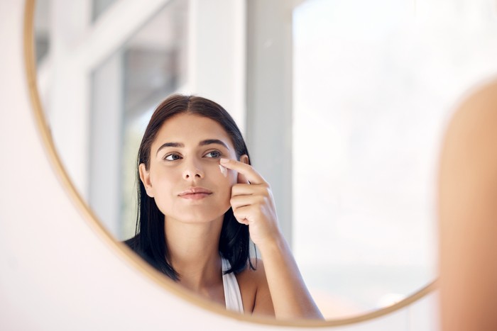 Mirror reflection of woman with skincare cream, spa lotion or dermatology ointment for melasma or acne treatment. Bathroom facial routine, healthcare and face of girl apply cosmetics beauty product