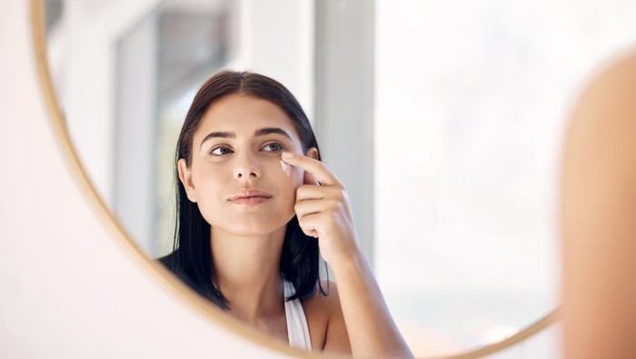 Mirror reflection of woman with skincare cream, spa lotion or dermatology ointment for melasma or acne treatment. Bathroom facial routine, healthcare and face of girl apply cosmetics beauty product