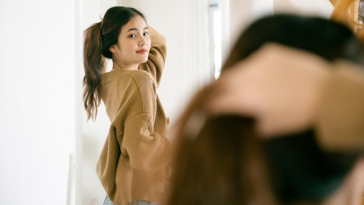 Young beautiful asian woman happily dressed in front of the mirror. She looks good and has confidence in herself