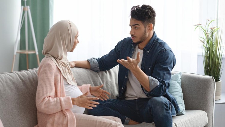 Pregnancy And Relationship Problems. Pregnant Muslim Spouses Arguing At Home, Expectant Muslim Lady In Hijab And Her Arab Husband Quarreling While Sitting On Couch In Living Room, Free Space