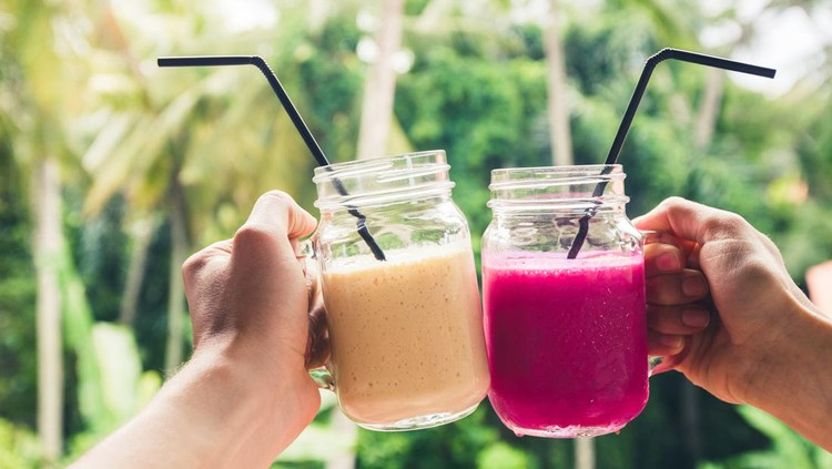 Two colorful fruit shakes in hands. Summer and tropical mood. Cold blended drinks, banana and dragon fruit smoothie. Clink glasses by couple hands