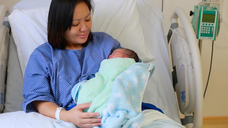 Pregnant young woman lying on the bed in delivery room. Side view of happy pregnant female resting on bed in hospital ward. Healthcare and pregnancy concept