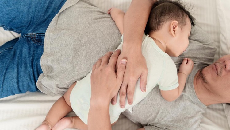 Top view of cute Asian baby boy sleeping on his father's chest. Asian father and baby sleeping together at home, father holding and embracing his son in arms.