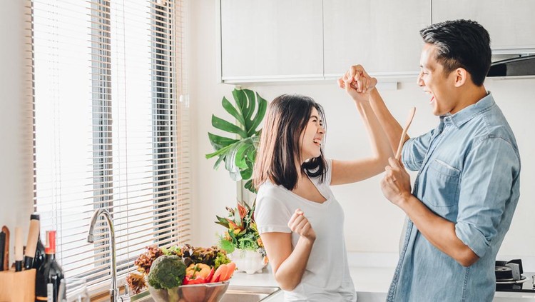 Romantic Asian couple in love is dancing and smiling while cooking together in kitchen