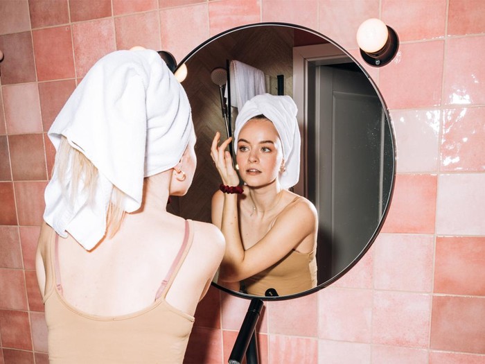 Foto seorang perempuan yang terlihat sedang memakai skincare untuk kulit wajahnya.