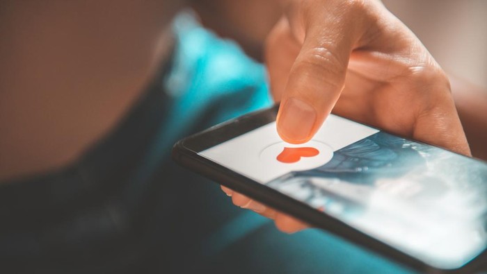 Finger of woman pushing heart icon on screen in mobile smartphone application. Online dating app, valentine's day concept.