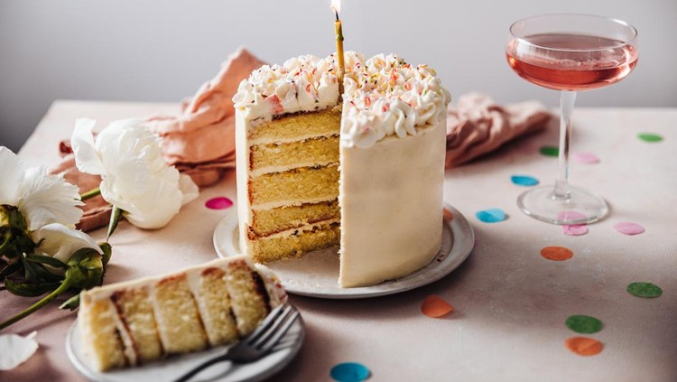 1247903563 Homemade layered cake decorated with cheese cream icing and multi colored sugar sprinkles. Beautiful birthday cake with candle on a table.