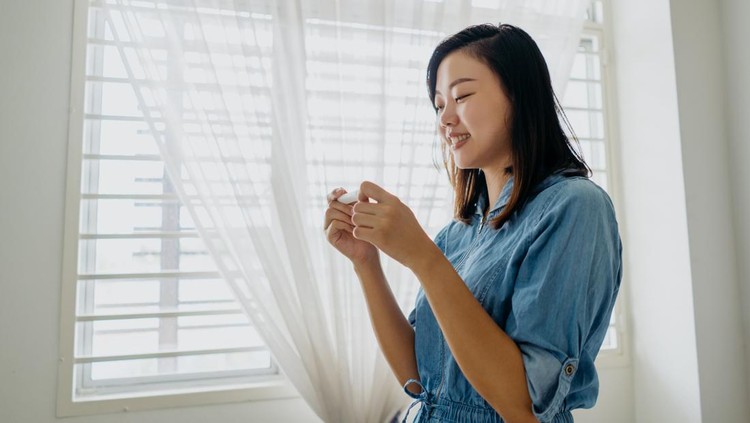 Image of a smiling Asian woman holding a pregnancy test kit and looking at the test result