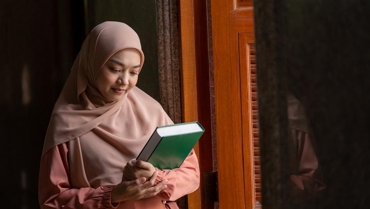 Beautiful Muslim girl in hijab reading Quran in mosque