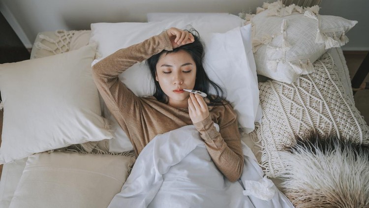 directly above Asian Chinese Woman lying on bed covered with blanket having  cold and flu measured her body temperature with digital thermometer