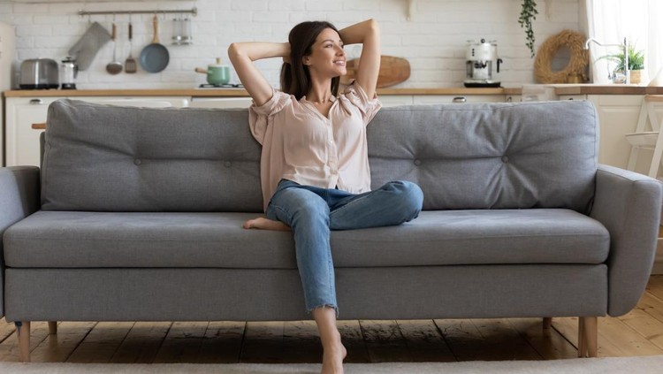 1171789127 In cozy living room happy woman put hands behind head sitting leaned on couch 30s european female enjoy lazy weekend or vacation, housewife relaxing feels satisfied accomplish chores housework concept