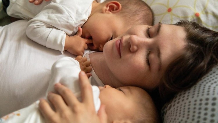 Menyusui bayi kembar Happy mother lying in bed with baby daughters in the morning